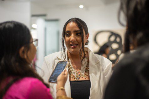 Shipra Sharma wearing a pearl necklace talking to a reporter in a pink suit.