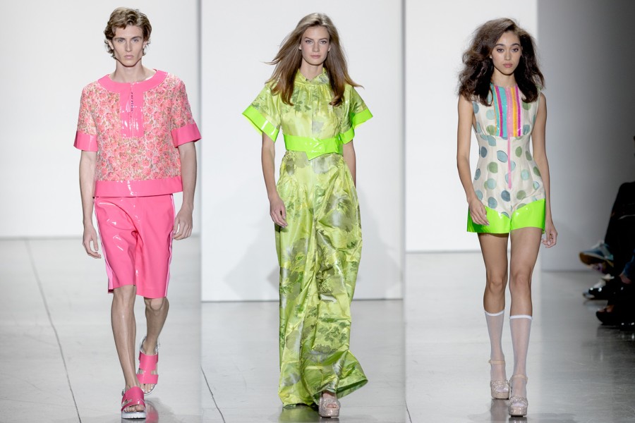 From left to right: A male walks in a pink shirt and shorts; a female model walks in a light green gown; a female model walks in a polka dot dress