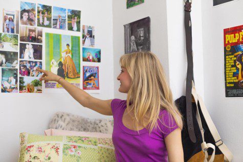 Catherine Desciak smiles as she points towards the wall of posters above her bed. Catherine is wearing a purple t-shirt with dark blue jeans.