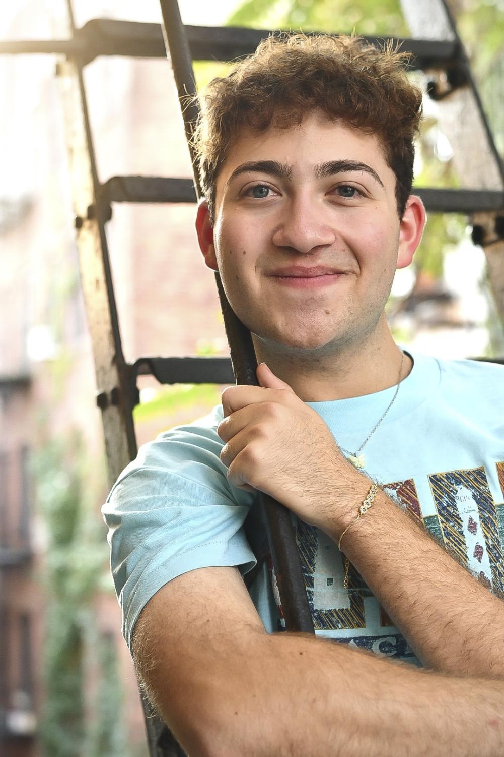 Ryan Wasserman, a Tisch student majoring in theater, poses for the camera on a fire escape wearing a blue t-shirt.