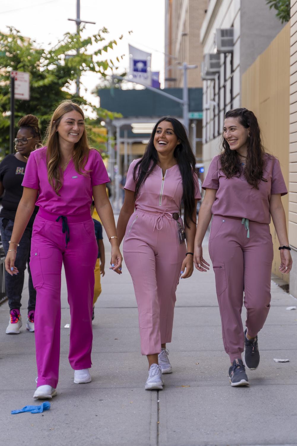 Danielle Mark (left), Shannon Partovi (middle) and Daniella Babayev (right) are conversing as they walk outside of a Meyers building. They are all wearing pink scrubs.