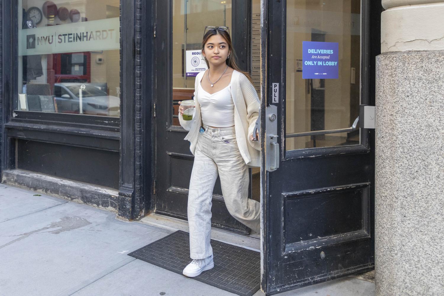 Miu Sato walks outside of a Steinhardt building wearing a patterned white tank top, white cardigan and white printed jeans.