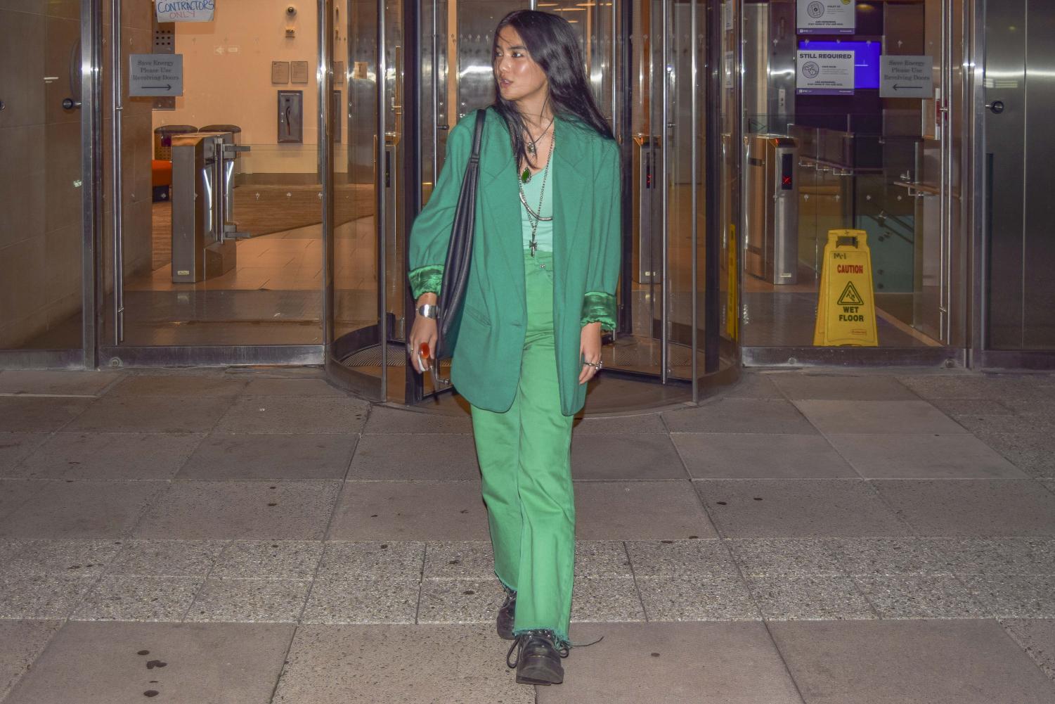 Isabella Yang walks out of a Stern building wearing green trousers, a green tank top, a green jacket and silver jewelry.
