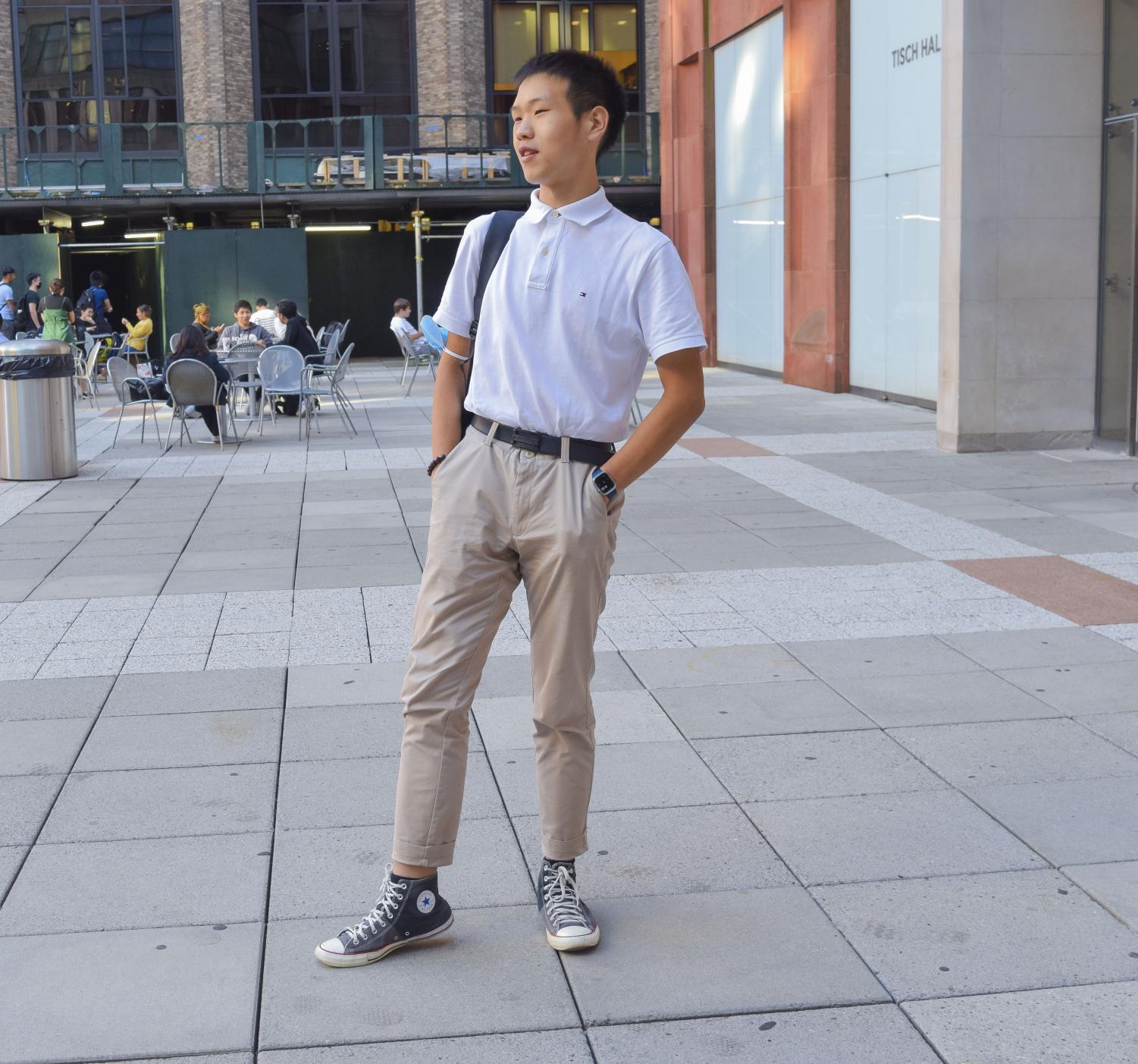 Kevin Chen stands in front of a Stern building wearing a white polo shirt, a black belt and khaki pants.