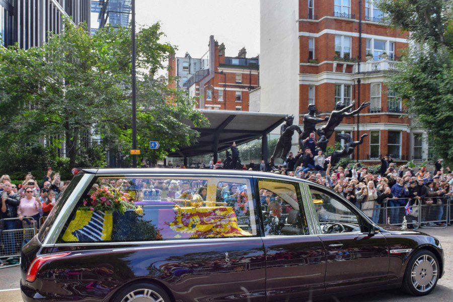 Queen+Elizabeth+II%E2%80%99s+burgundy+red+Jaguar+Land+Rover+hearse+passes+by+crowds.+Behind+the+hearse%E2%80%99s+clear+glass+window+lies+the+late+queen%E2%80%99s+decorated+oak+coffin.