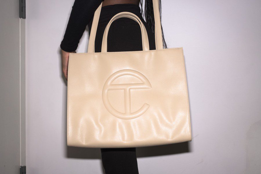 A female model dressed in black against a white background wears a nude Telfar bag.