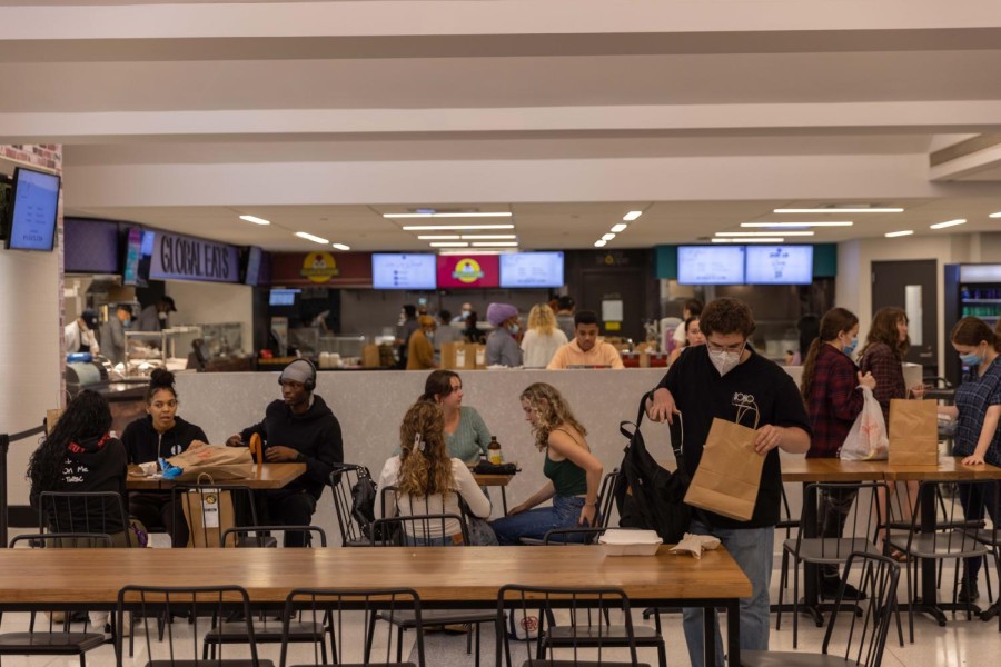 Dining tables and chairs in the foreground and food court vendors in the background.