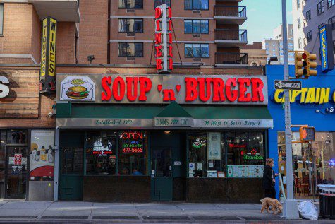 The facade of a restaurant with green accent color and light sign with text “SOUP ‘n’ BURGER” in red. “