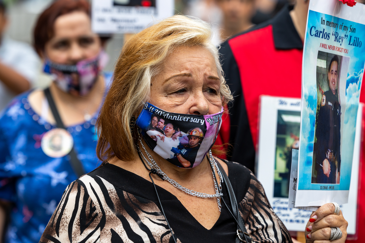 Mother of Carlos “Rey” Lillo, an officer who died during the Sept. 11 attacks, wears a Sept. 11 commemorative mask and holds a sign with a picture of her late son.