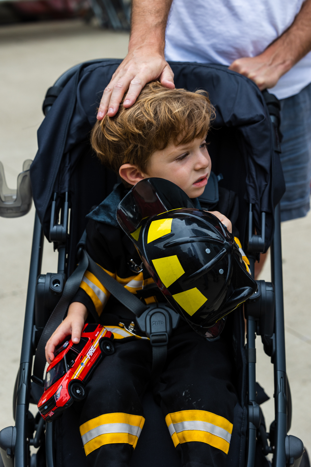 An infant boy sits in a stroller dressed in a firefighter costume.