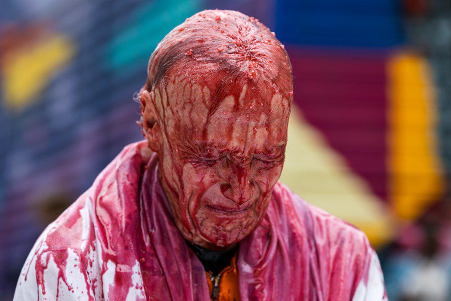A performance protestor whose body is covered in red liquid has a pained facial expression.