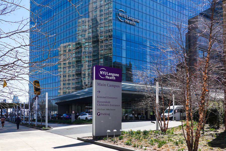 The outside entrance of N.Y.U Langone Health’s main campus with a road sign in front of the modern building with a glass facade.