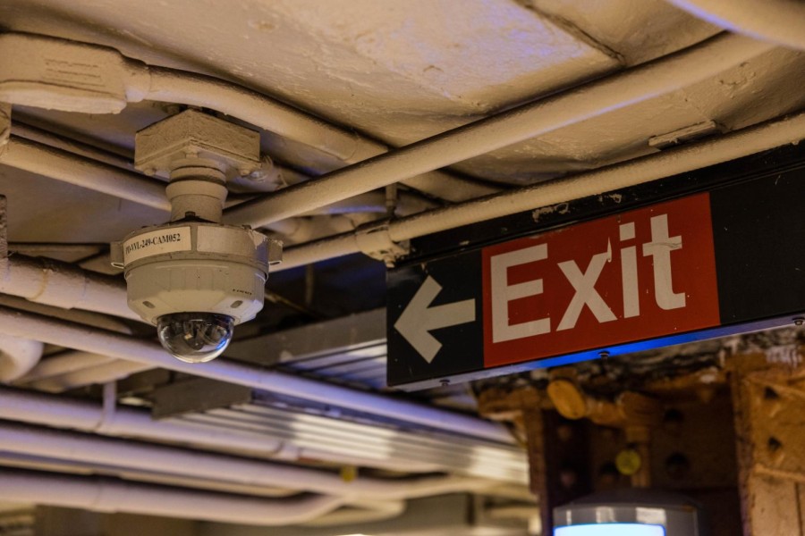 The ceiling of the 14th Street-Union Square station. To the left is a surveillance camera; to the right is a red “Exit” sign.