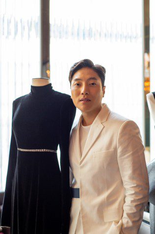 Andrew Kwon poses next to a mannequin in a black dress.