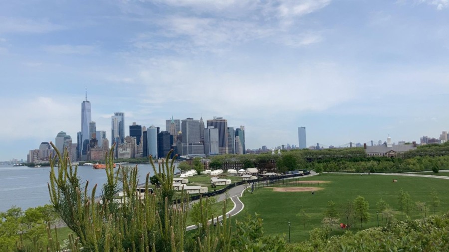 A panoramic view of the greenfield at Governors Island, with the Manhattan skyline visible in the background.