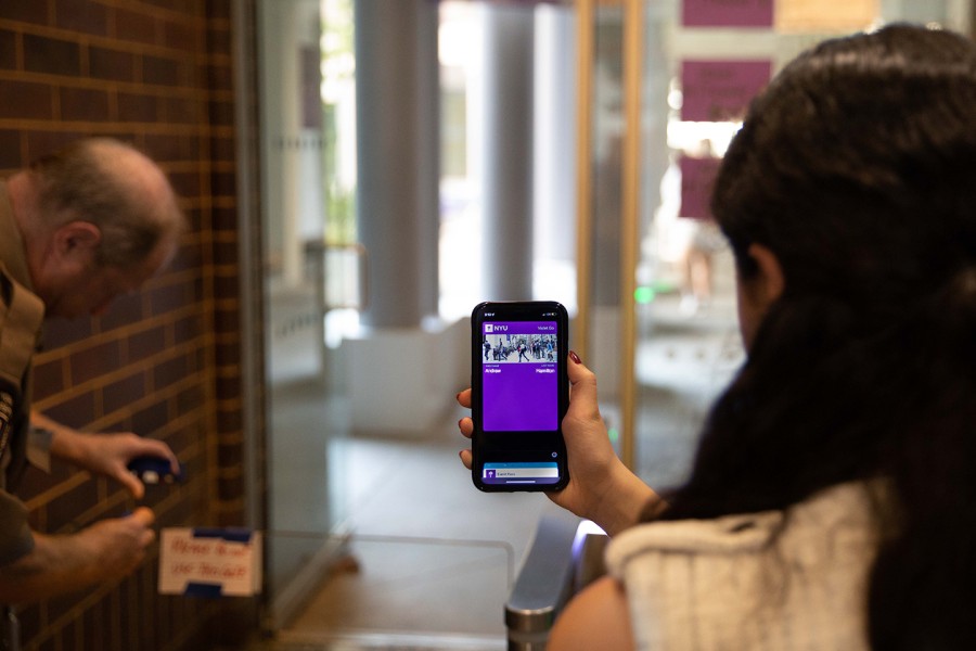 A student holds up their phone displaying a purple Violet Go pass to enter an NYU building.