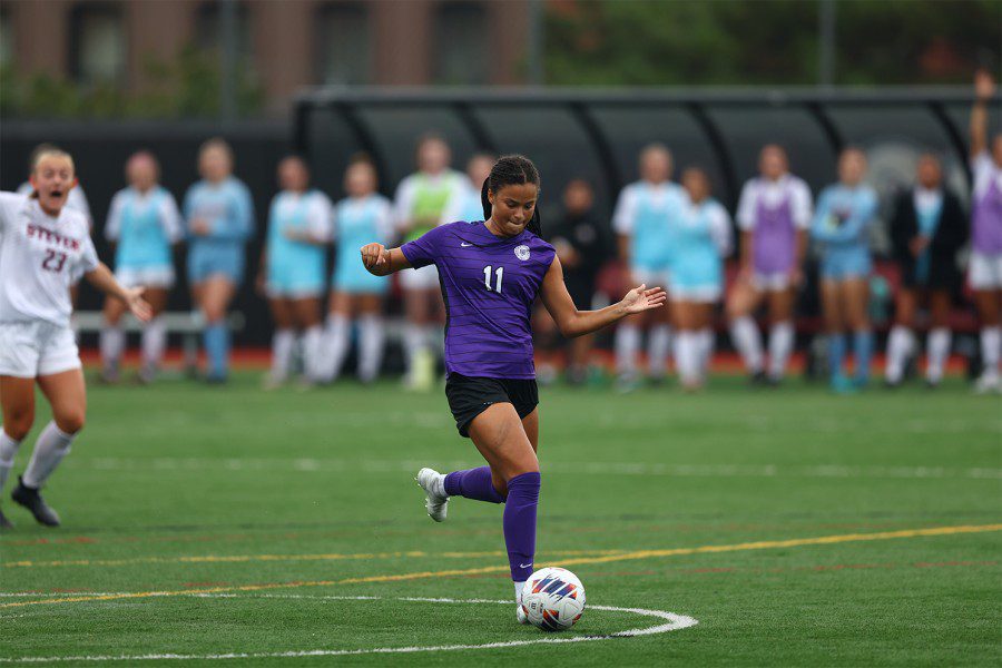 A member from the New York University women’s soccer team kicks the ball down the soccer field.