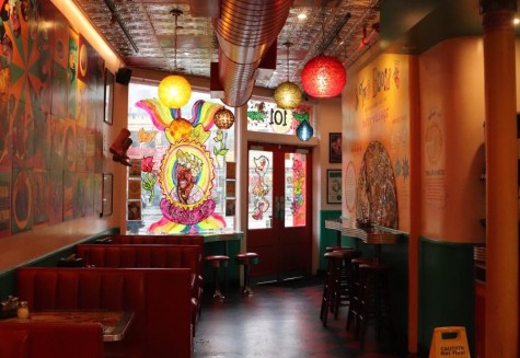 The interior view of Two Boots restaurant. To the left there are red booths for sitting, and stained glass art is visible at the entrance.