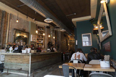 The interior of a restaurant with green walls and a bar counter. The room is lit by warm-hued light bulbs. People sit at tables eating.