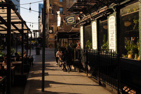 The outdoor dining area on the street outside a cafe with green walls and a plaque with text “KOBRICK COFFEE CO. EST. NYC 1920.”