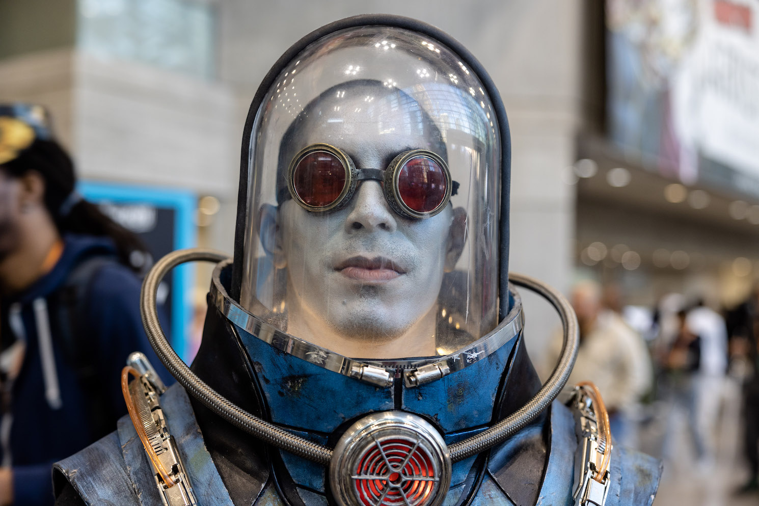 A blue-faced cosplayer wearing a pair of red goggles and a glass-finished hazmat suit.