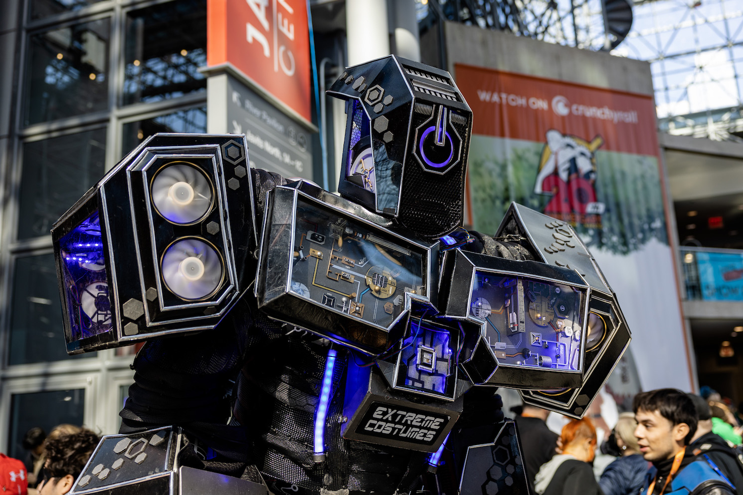 A cosplayer wears a black-and-purple robot costume accented with purple designs that look like wires and buttons. The text on the center of the outfit reads “EXTREME COSTUME.”