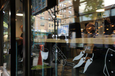 A shot of the exterior window of Dorado Tacos & Quesadillas, located on 28 E. 12th Street. A taco, burrito, chips and chiles are printed on the window.