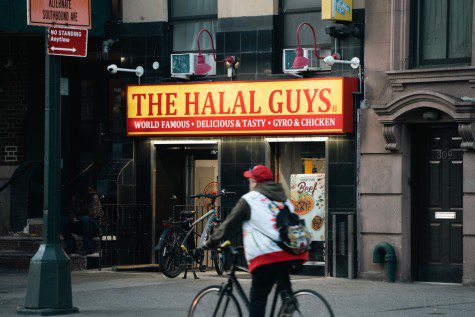 A man on a bike passes by the exterior of The Halal Guys, located on 307 E. 14th Street.