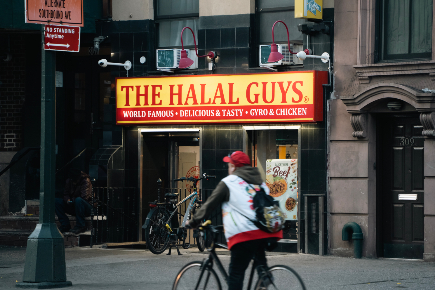 A man on a bike passes by the exterior of The Halal Guys, located on 307 E. 14th Street.