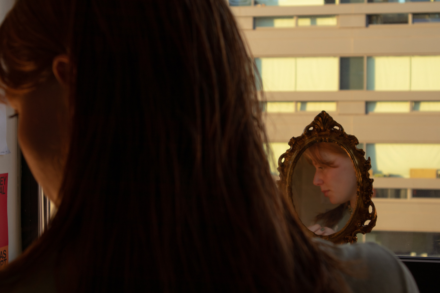 A girls looks onto the ground in front of a makeup mirror in her dorm room.