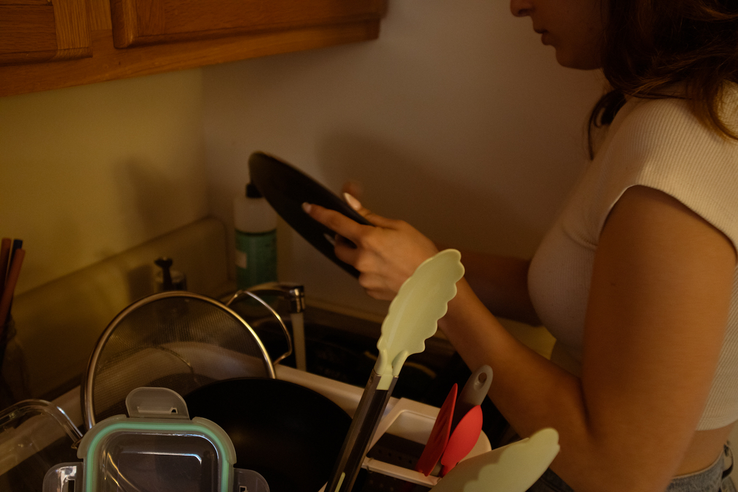 A person washing a plate with a sink full of dishes.