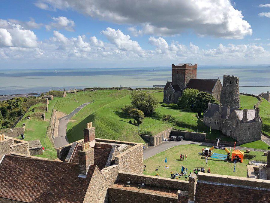 Landscape photo of Dover, England, featuring stone buildings, greenery and an ocean in the background.