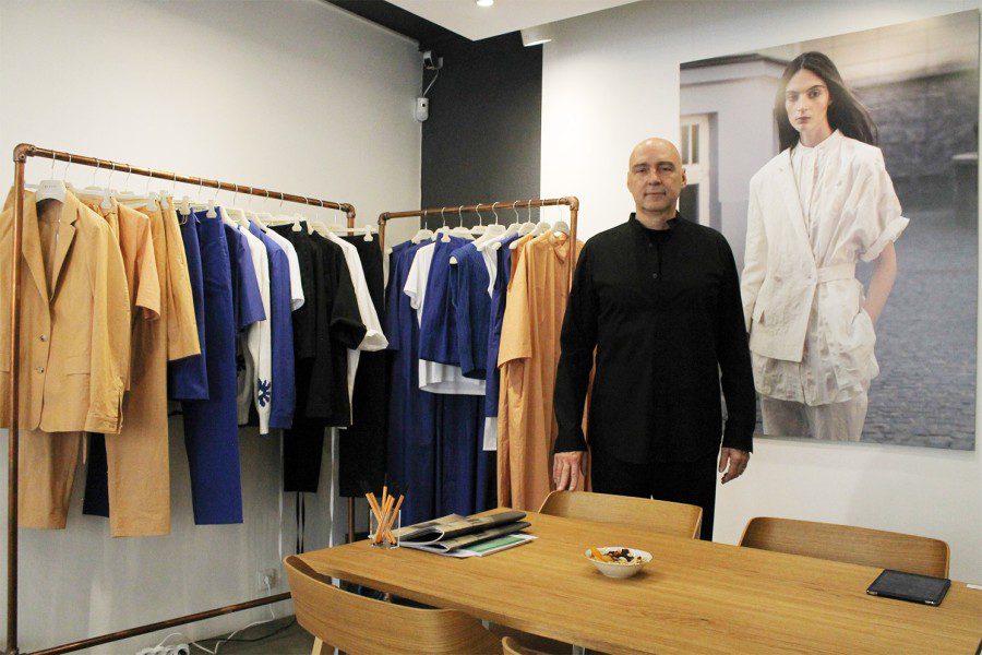 CEO of Nehera Ladislav Zdut poses in front of two racks of business casual clothing and a poster of a model.