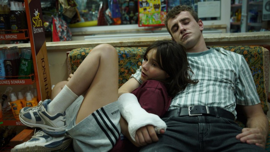 A man with a plastered right arm wraps his hand around a girl who leans her back against the man. The two are on a couch in a convenience store.
