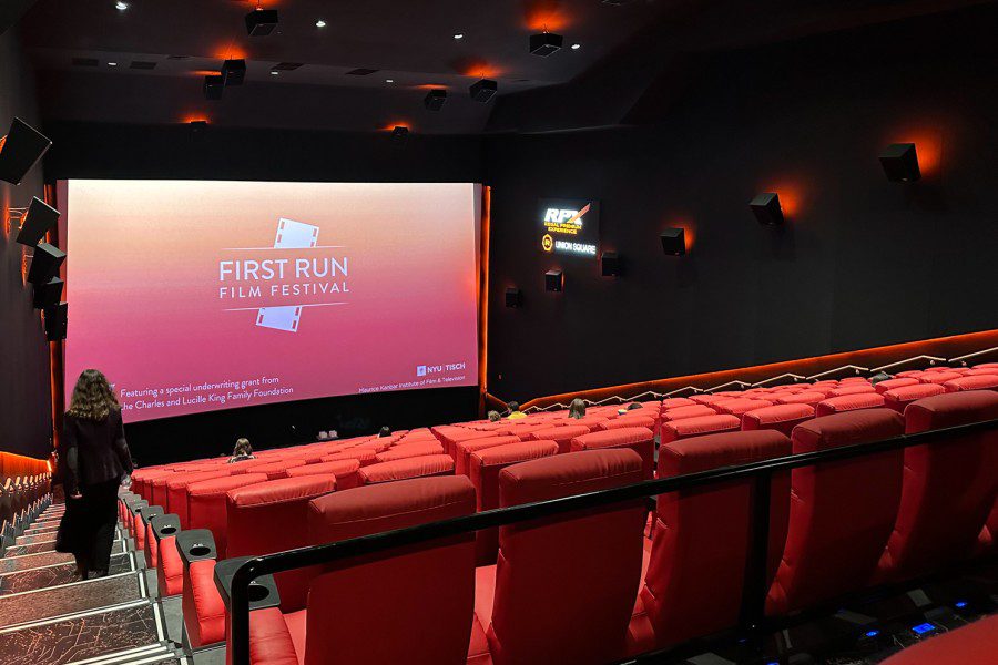 A auditorium inside a cinema with red chairs and the text “FIRST RUN FILM FESTIVAL” projected onto the backdrop screen.