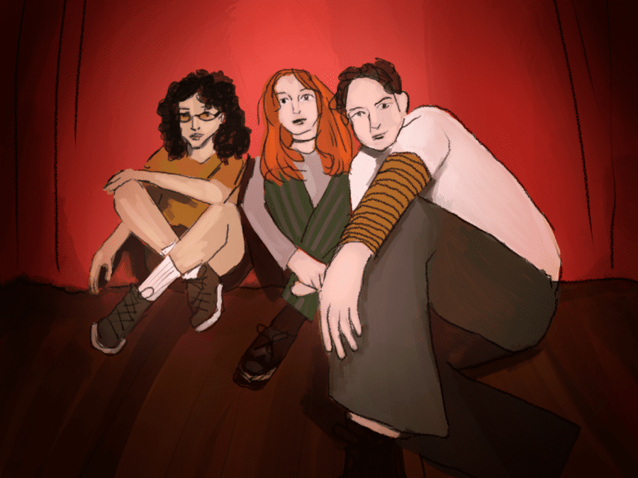 An illustration of Katie Gavin, Josette Maskin and Naomi McPherson posing for a photograph while sitting on a stage. McPherson, on the left, has brown curly hair, and wears yellow-tinted glasses, a yellow short-sleeved shirt, brown shorts, white socks, and brown lace-up shoes. Gavin, in the center, has red straight hair and wears a gray long-sleeved shirt, green pants with gray vertical stripes, and brown shoes with tied bows. Maskin, on the right, is wearing a white T-shirt, an orange long-sleeved shirt with brown stripes under the white shirt, gray-ish brown pants, and dark shoes.
