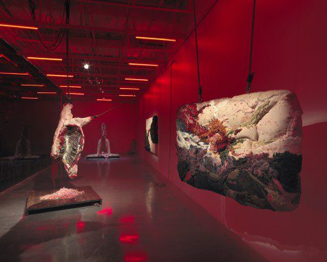 Four large pieces of art on display in an exhibition venue lit up with red light.