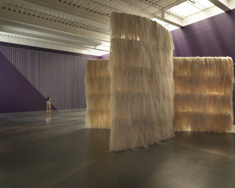 A large white art installation on display in an exhibition venue with purple walls and white ceiling.