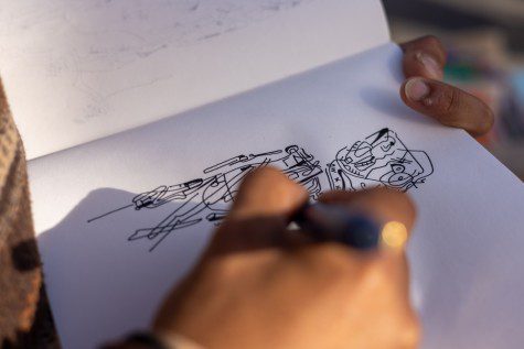 Two hands holding a sketchbook and a pen. The artist, Antonio Garcia, who is off-camera, is sketching a figure with a pen.