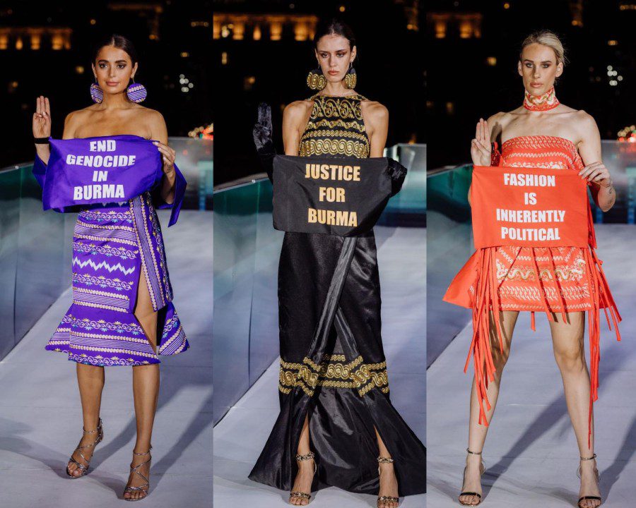 From left to right: a model walking down the runway in a purple dress holding a sign that is purple and reads in white font, “End Genocide in Burma”; a model walking down the runway in a black dress with gold details holding a sign that is black and reads in gold font “Justice for Burma”; and a model walking down the runway in an orange dress holding a sign that is orange and reads in white font “Fashion is Inherently Political”.