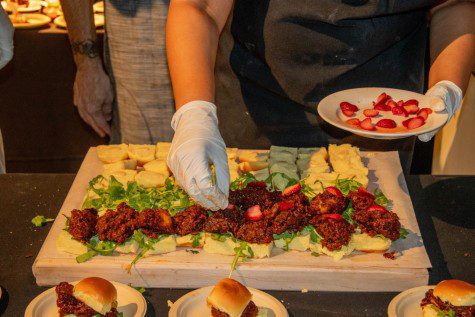 A person places cut strawberries onto a tray of hamburger sliders. The strawberries are an ingredient of the sliders.