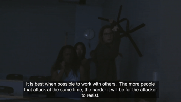A moving GIF image of three people holding up chairs as weapons in a dark room with subtitle “It’s best when possible to work with others. The more people that attack at the same time, the harder it will be for the attacker to resist. Separate the attacker from their weapon when you can, but do not pick up the weapon.”