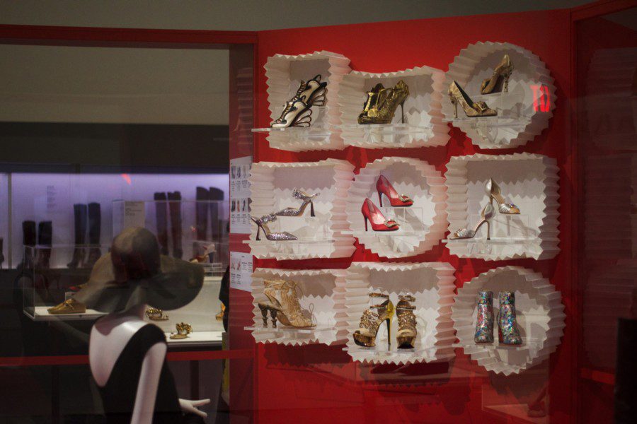 Nine pairs of shoes of varying styles displayed inside nine paper cases hung against a red background.