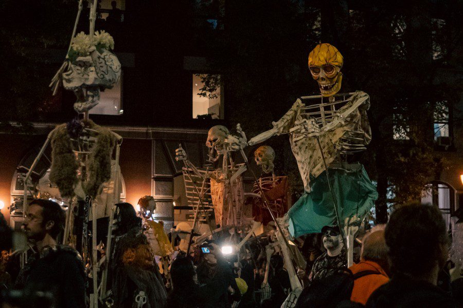 Large skeletons on stilts walking through a crowd of people. The skeletons have articles of clothing and drawings on them.