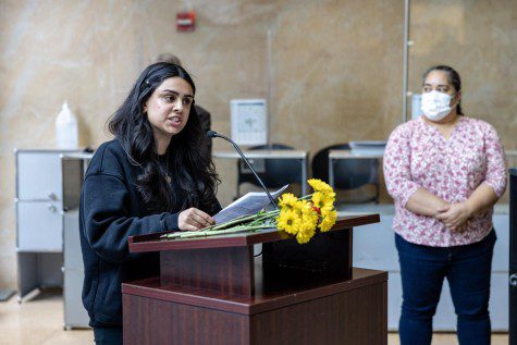The vice president of New York University’s Persian Cultural Society Kiana Naderi speaks behind a wooden podium with a bouquet of yellow flowers placed on it.