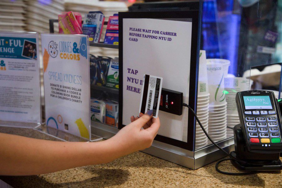 A hand holding an N.Y.U. identity card up to a dining hall entrance scanner.