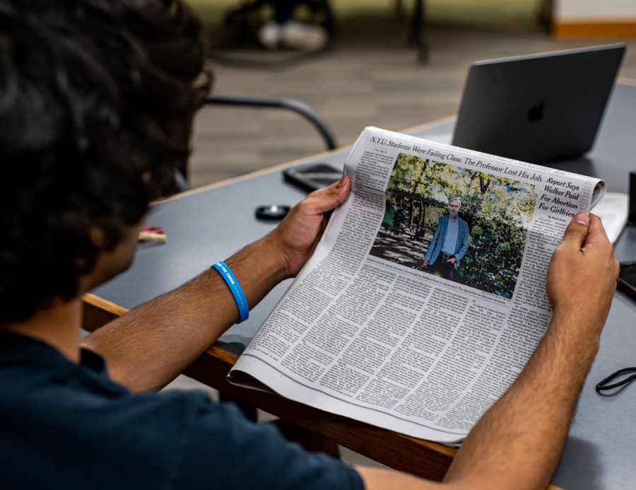 A man reading the October 4, 2022, edition of The New York Times. The newspaper headline reads “N.Y.U. Students Were Failing Class. The Professor Lost His Job.”