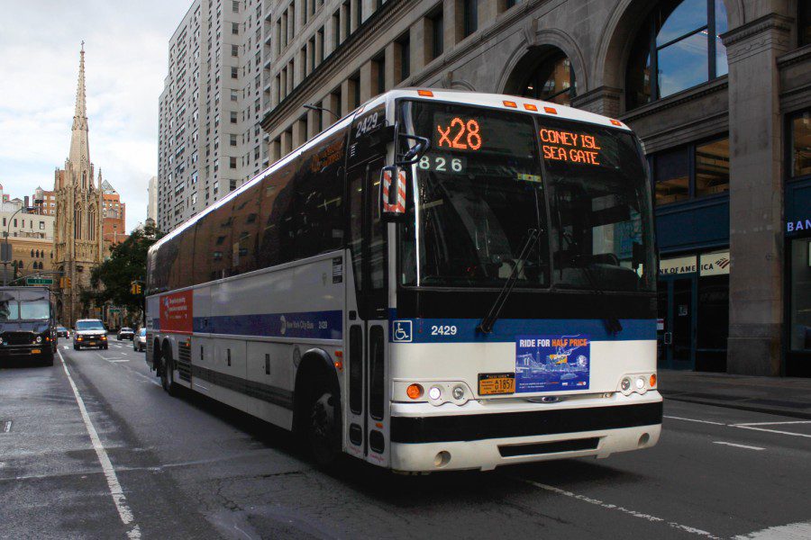 An M.T.A. bus with white and blue stripes driving down Broadway.