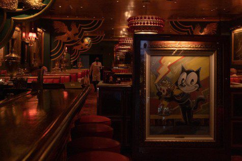A painting of Felix the Cat holding a tea kettle sits in front of a restaurant decorated in red.