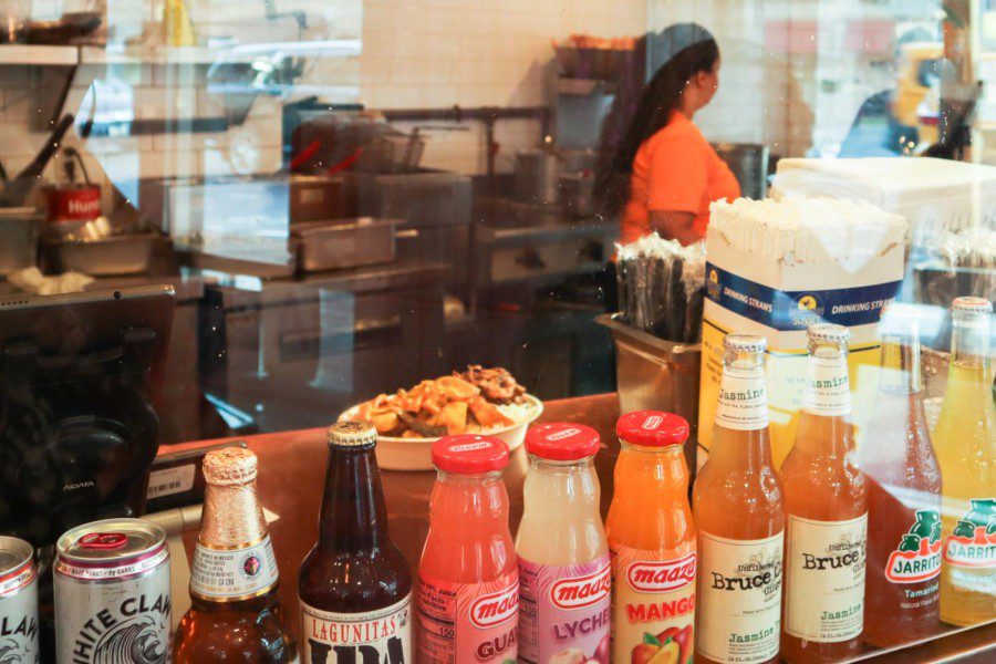 A woman stands behind the counter making a dish at Taco Mahal. Various drinks are on display in the window.
